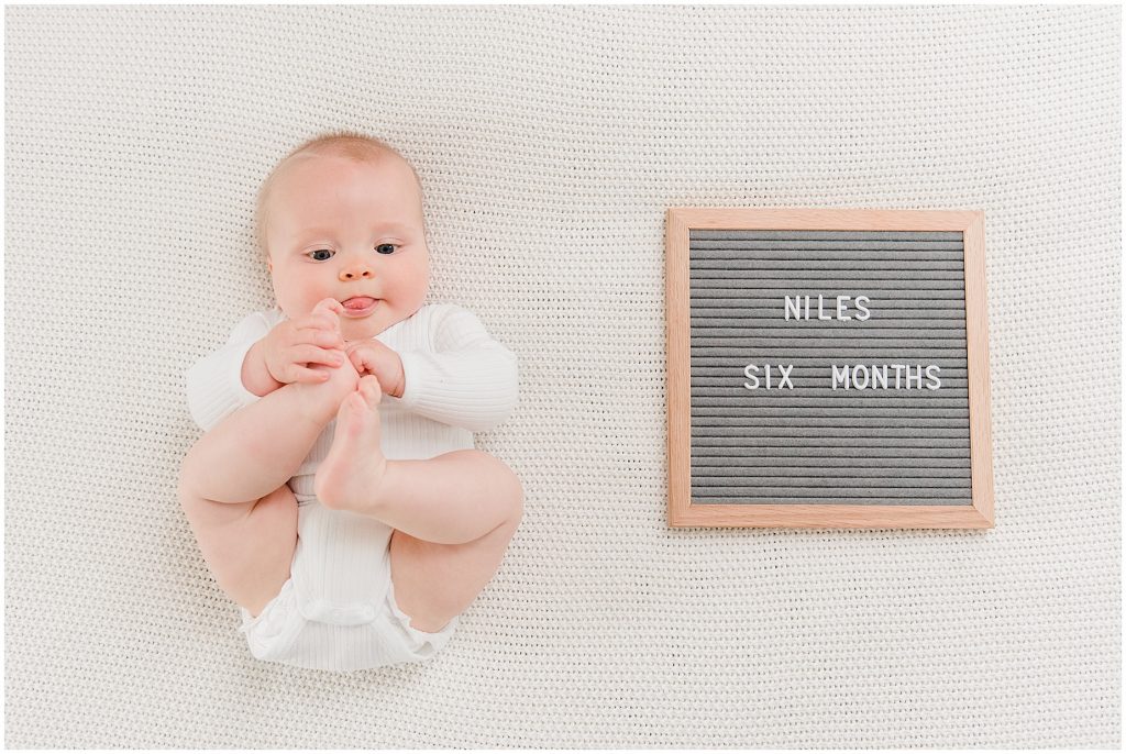 Richmond photographers niles turned 6 months lying down eating his foot with letter board 