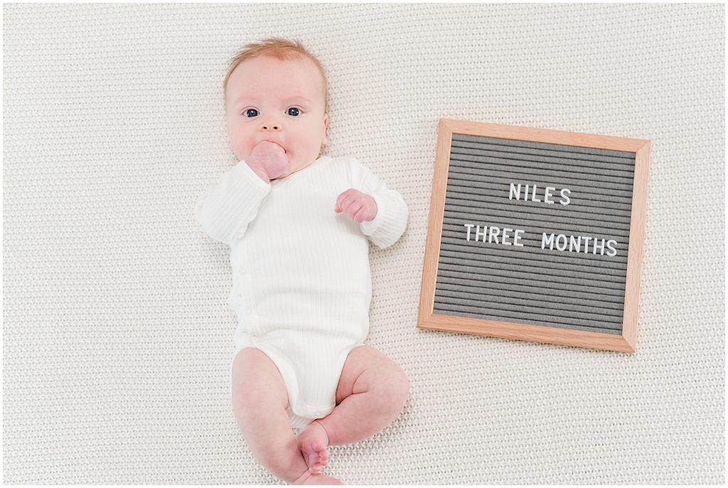 Richmond photographers niles lying on bed at 3 months with letter board