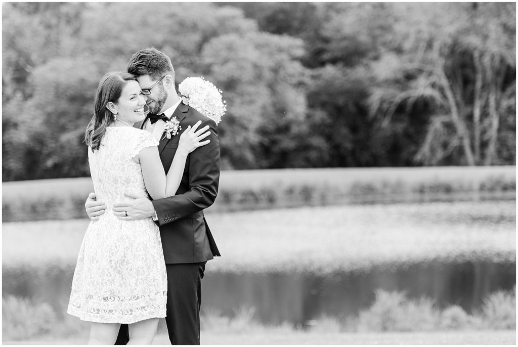 Bride laughing and groom wrapped up together in front of lake at barn at edgewood