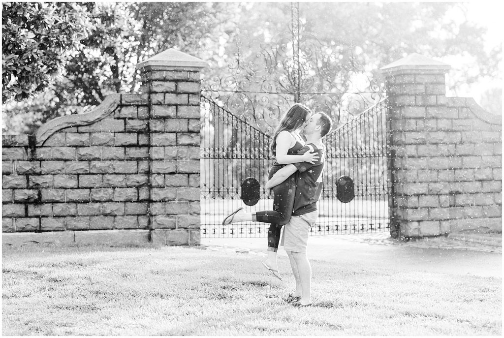 rainy engagement session guy picking up girl at maymont park gate in virginia tech gear