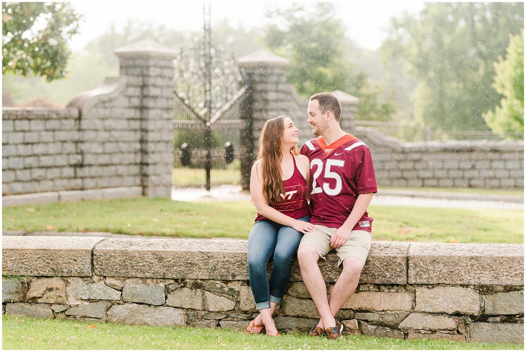 engagement session couple sitting at maymont park gate in virginia tech gear while it rains