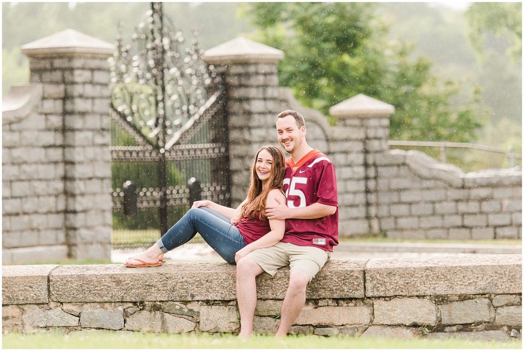 rainy engagement session couple sitting at maymont park gate in virginia tech gear