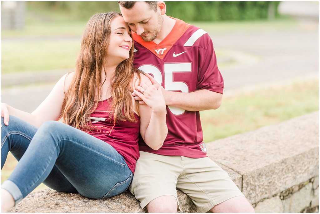rainy engagement session couple sitting at maymont park gate in virginia tech gear