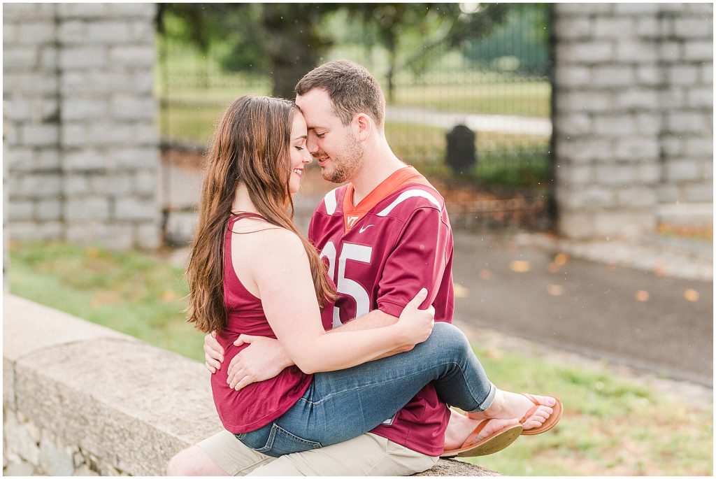 rainy engagement session couple sitting on each other in virginia tech shirts