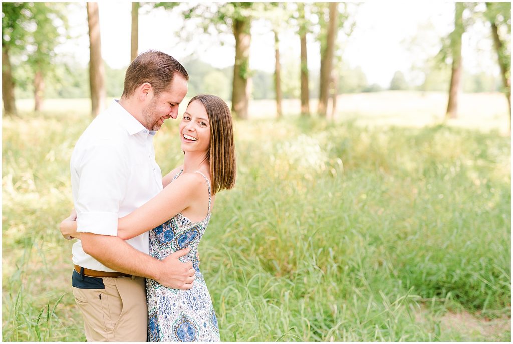 sunny Lansdowne resort engagement session couple in grassy field surrounded by trees at a golf course in Leesburg