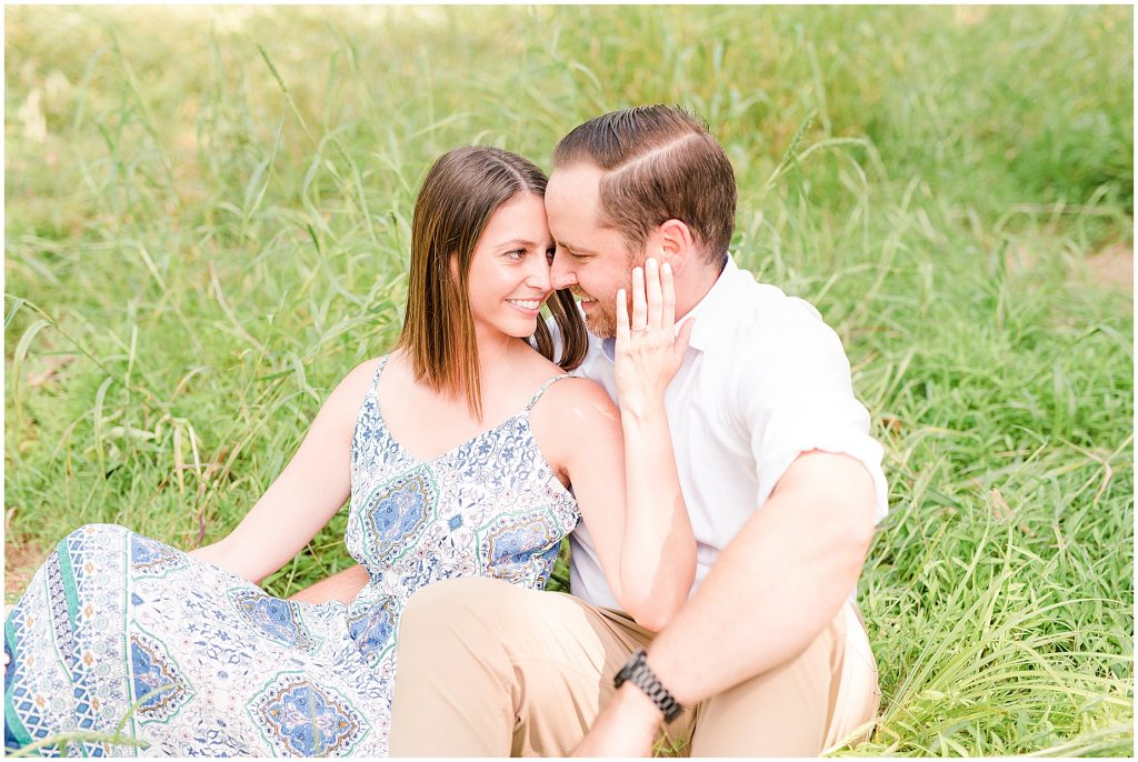 sunny Lansdowne resort engagement session couple sitting in a grassy field at a golf course in Leesburg