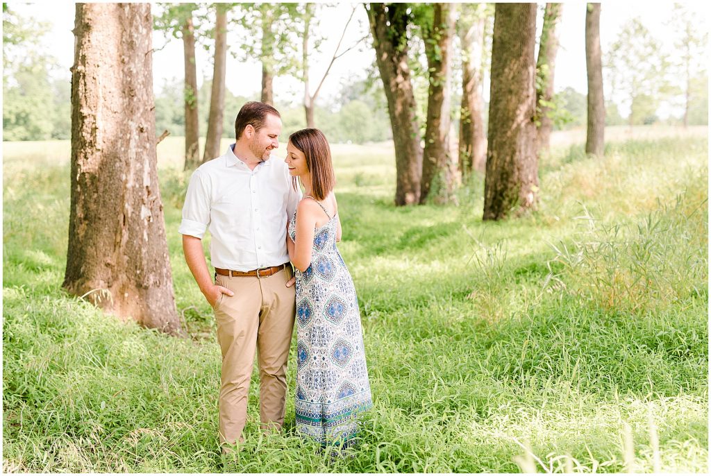 sunny Lansdowne resort engagement session couple in grassy field surrounded by trees at a golf course in Leesburg