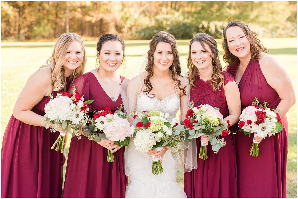 bride and bridesmaids in maroon dresses outdoor fall portraits at amber grove virginia wedding venue