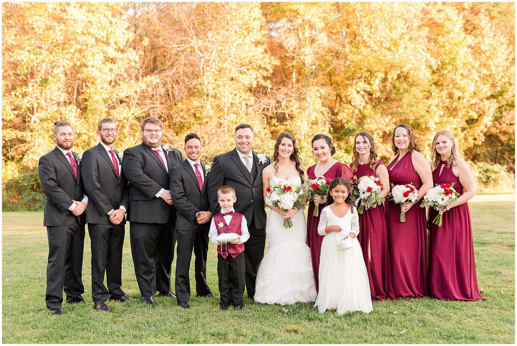 bridal party in maroon dresses and black suits walking in fall field at amber grove wedding richmond