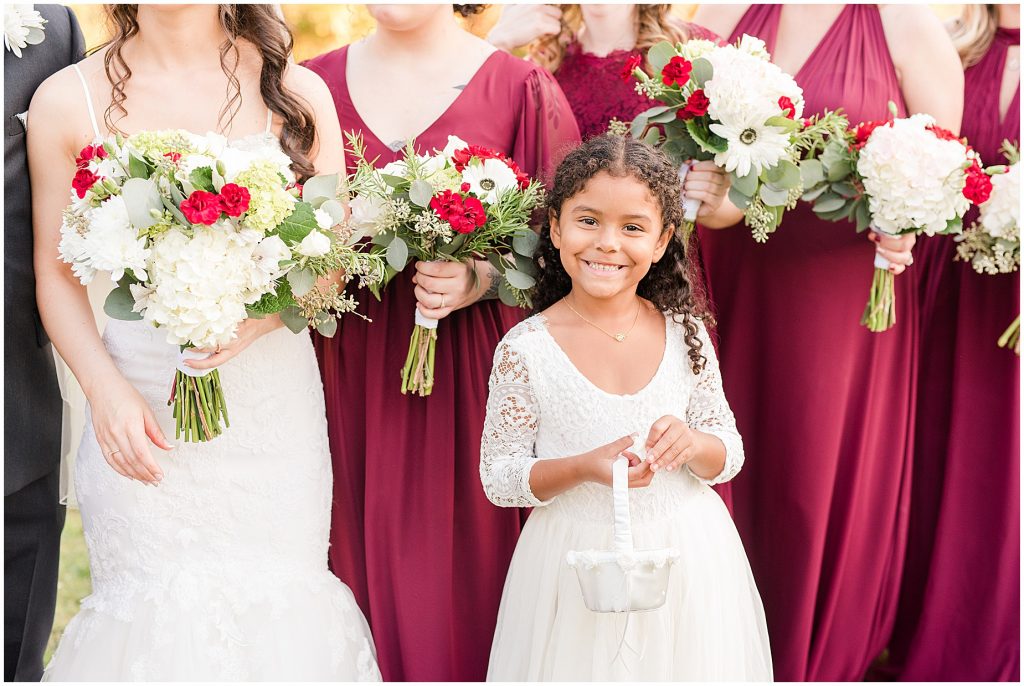 brided and bridesmaids in maroon dresses with flower girl in fall field at amber grove wedding richmond