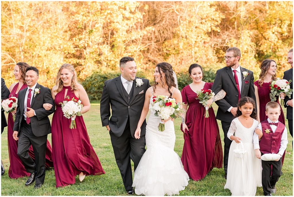 bridal party in maroon dresses and black suits walking in fall field at amber grove wedding richmond