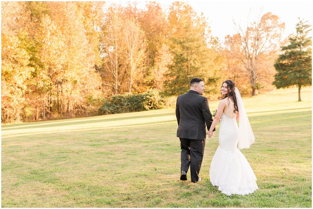 bride and groom walking in field surrounded by fall colored trees at Amber grove in richmond