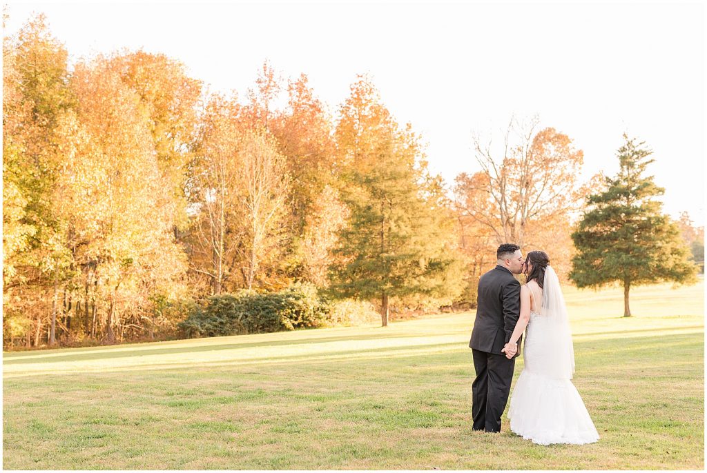 bride and groom in field with fall trees behind at amber grove in richmond