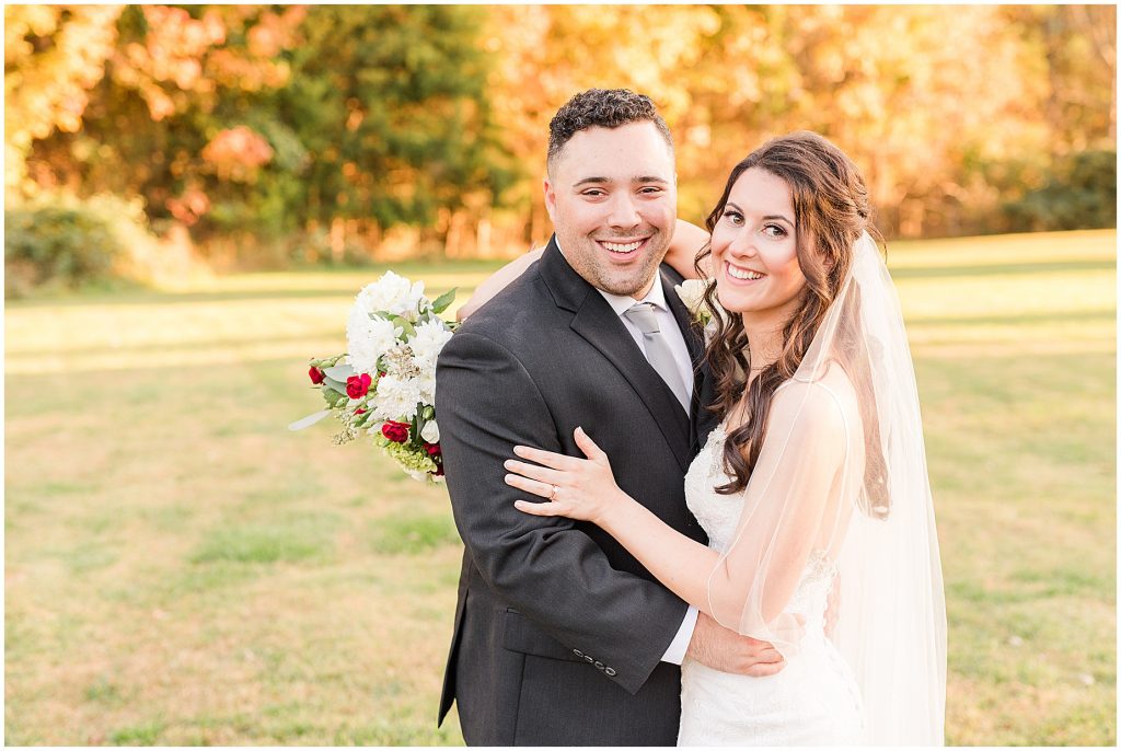 bride and groom smiling at camera in field surrounded by fall colored trees at Amber grove in richmond