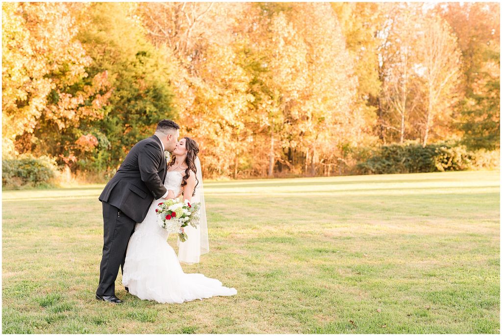 bride and groom kissing dip in field with fall color trees at Amber grove in richmond