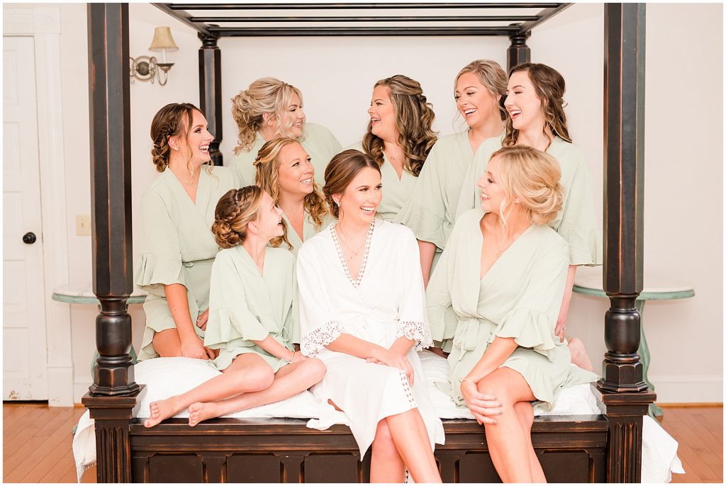bride and bridesmaids sitting on a bed in their robes laughing at waverly estate in southern virginia