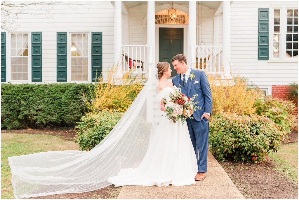 bride with long flowy veil with groom standing in front of plantation house at Waverly Estate in southern Virginia