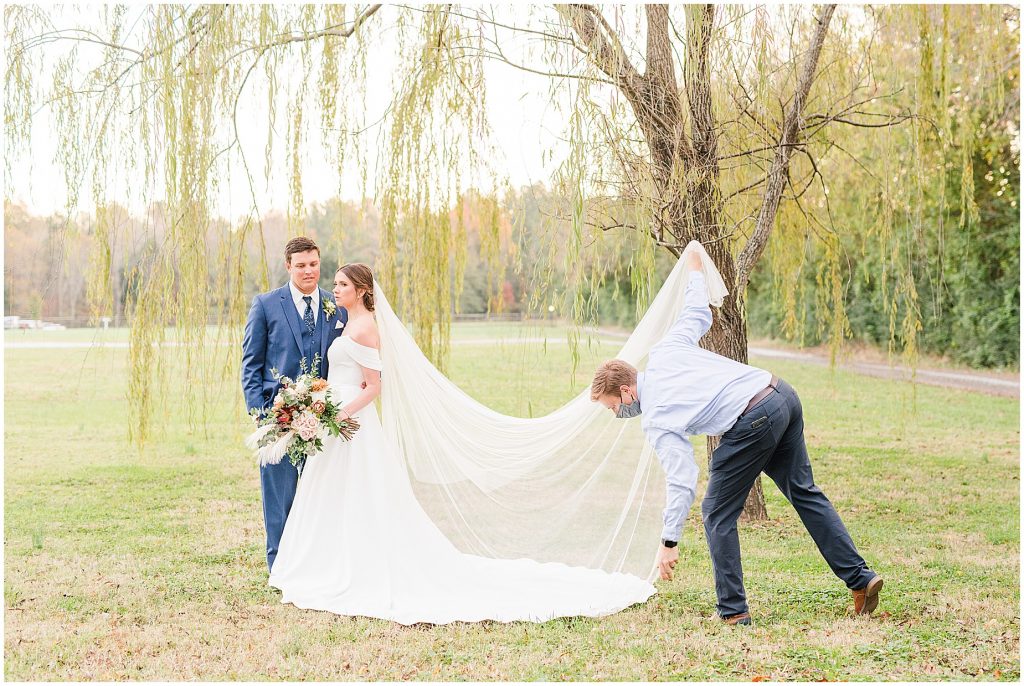 photographer holding a veil for bride and groom at Waverly Estate in Lunenberg, Va