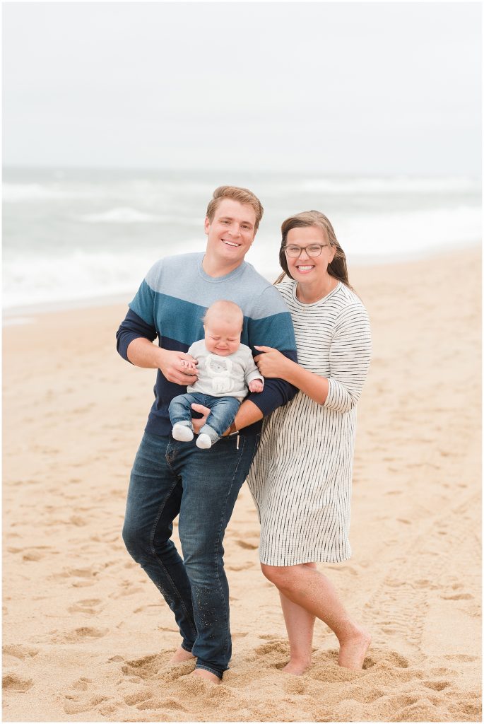 baby crying while family stand for a photo on the beach