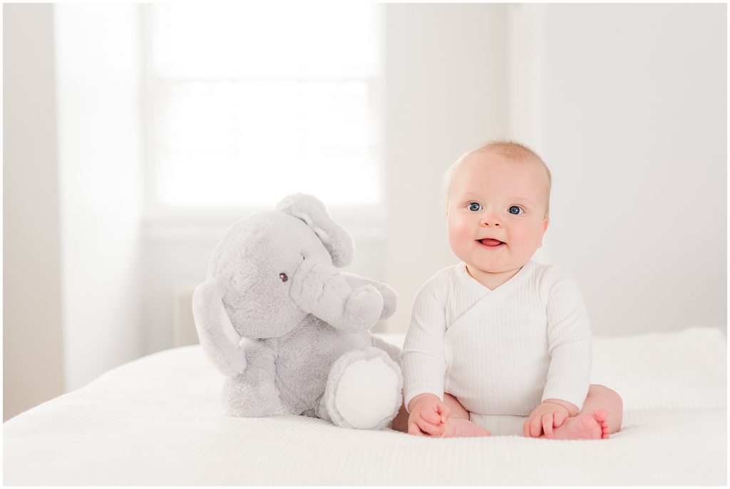 baby boy sitting on bed with stuffed animal elephant