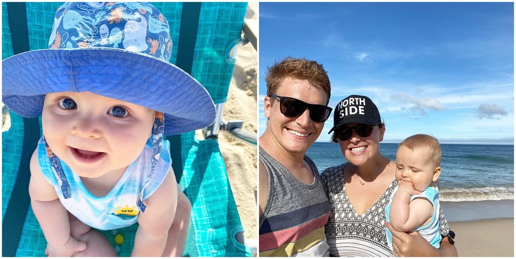 baby sitting at the beach with a hat and family standing for a photo