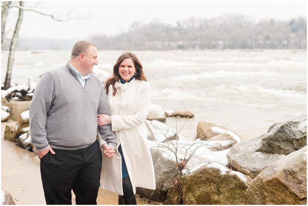 couple walking on belle isle in downtown richmond virginia for engagement session during the snow